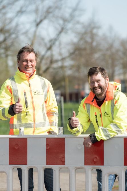 Zwei WiR-Mitarbeiter lehnen sich über einen Bauzaun